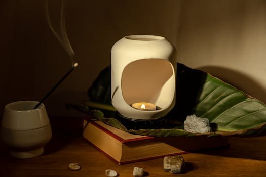 Tranquil aromatherapy scene with candle holder, incense, book, and natural elements for relaxation.