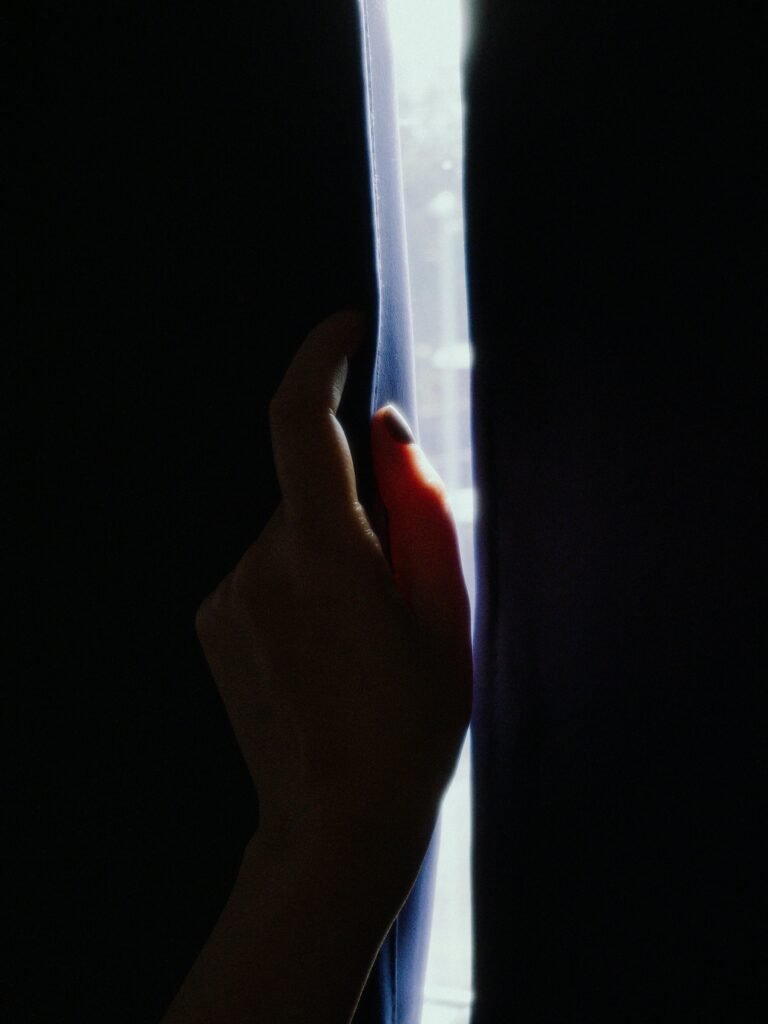 Mano sombreada abriendo cortinas oscuras, dejando que la luz entre en un plano vertical.
