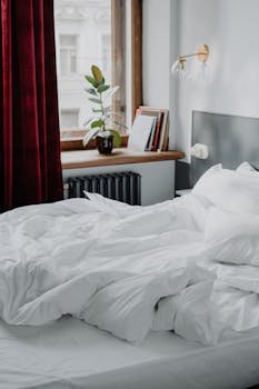 A serene bedroom with white linens, a window view, and a cozy atmosphere.