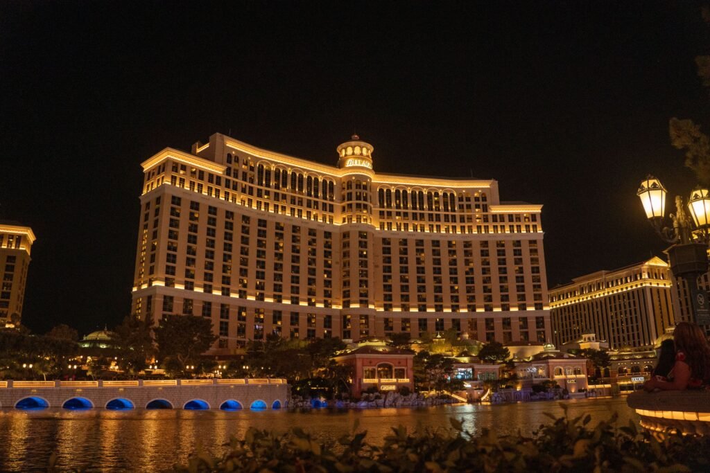 "Fotografía nocturna de la impresionante fachada iluminada del hotel y casino Bellagio en Las Vegas, perfecto para elegir el alojamiento perfecto  visto desde la zona de sus famosas fuentes sobre la laguna con arcos con luz azul. Un ejemplo icónico de alojamiento de lujo."