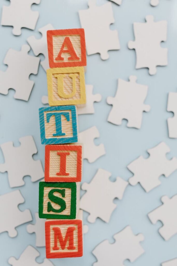 Colorful letter blocks spelling autism surrounded by puzzle pieces on a light surface.