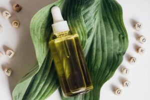 Una botella de aceite natural para el cuidado de la piel colocada sobre hojas verdes con bloques de letras que forman la palabra 'mañana'.