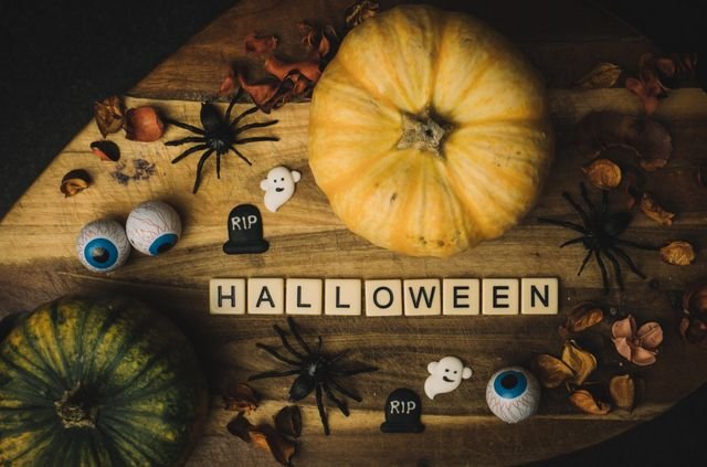 Halloween-themed flatlay featuring pumpkins, spiders, and eerie decorations on a wooden background.