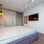 Spacious modern bedroom featuring a gray bed and wall-mounted TV with ambient lighting.