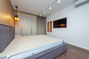 Spacious modern bedroom featuring a gray bed and wall-mounted TV with ambient lighting.